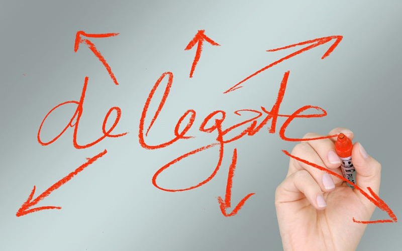 una mano sta scrivendo con un pennarello rosso la parola "delega" in inglese